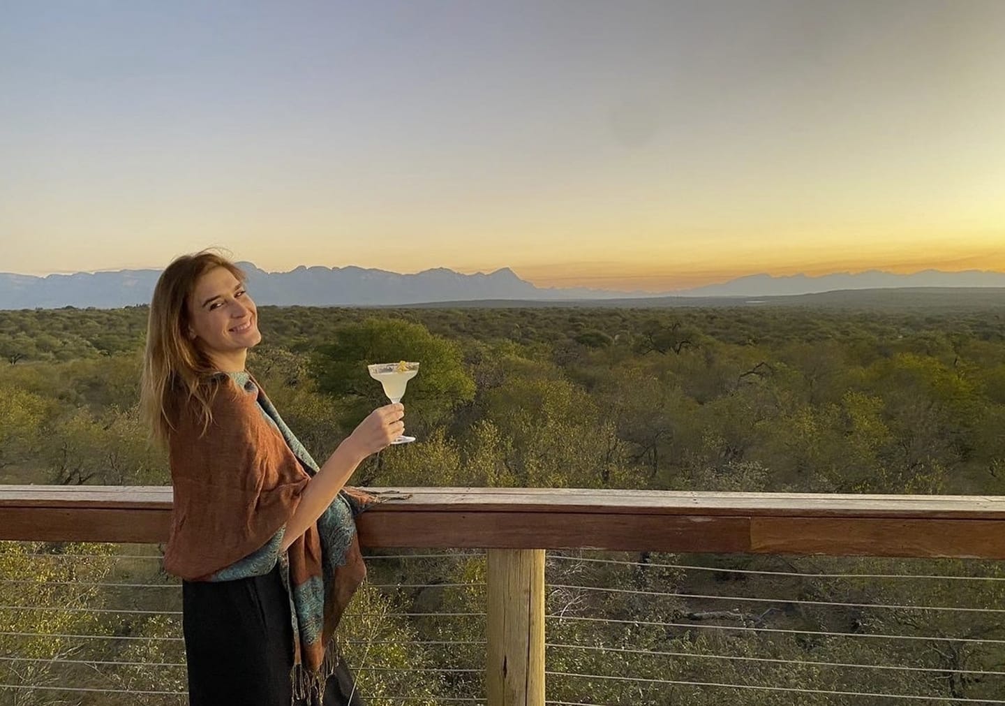 An Oase guest enjoys a sunset cocktail on the Sundowner Deck above the bush.